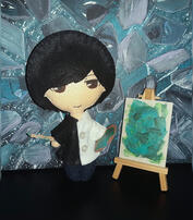 Saito Soma pintor Foto del muñeco de Saito Soma vestido de blanco y negro, sosteniendo un pincel y paleta de pintura (de cartón), junto a un pequeño atril con su "lienzo" de pintura verde.