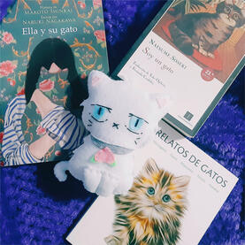 Hakuto Foto del muñeco de Hakuto, es un gato blanco con ojos celestes y un colla en forma de melocotón. Hay tres libros sobre gatos junto al muñeco.